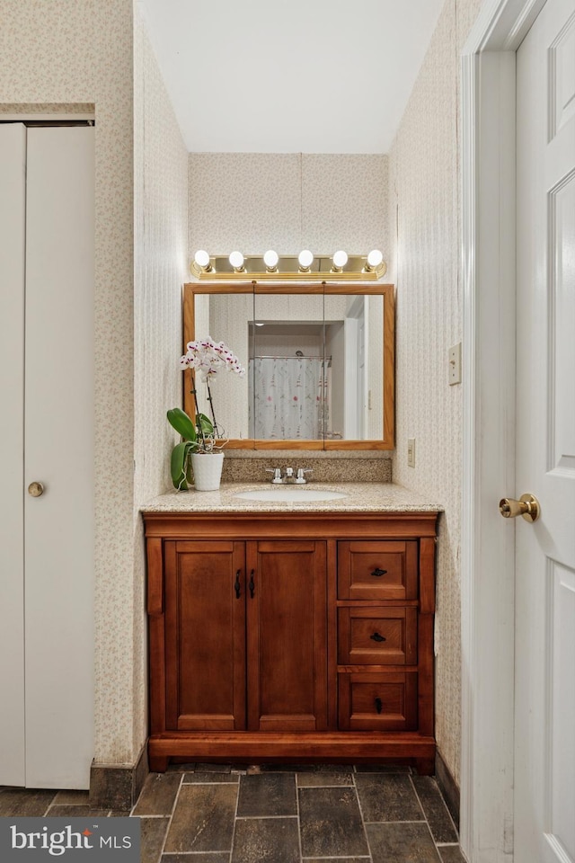 full bathroom featuring wallpapered walls, a shower stall, stone finish floor, and vanity