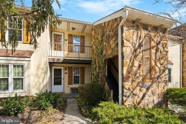 view of front of home featuring stone siding, a balcony, and stucco siding