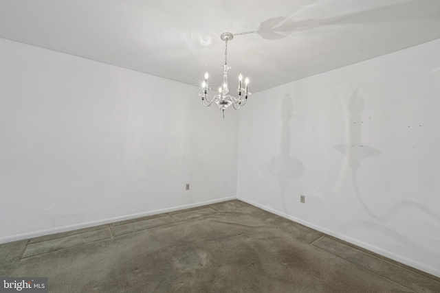 carpeted empty room with an inviting chandelier and baseboards