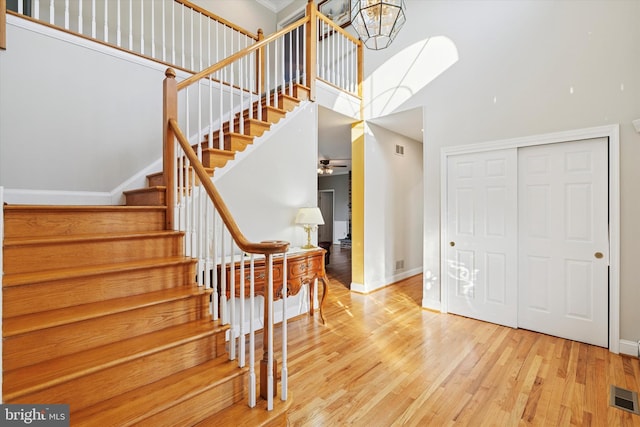 staircase featuring visible vents, a towering ceiling, baseboards, and wood finished floors