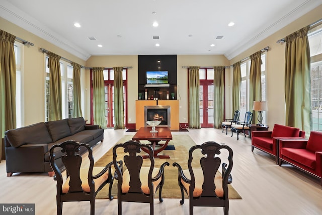 interior space featuring ornamental molding, light wood-type flooring, a glass covered fireplace, and visible vents