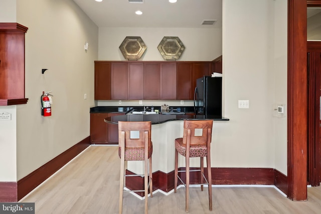 kitchen with light wood-style floors, freestanding refrigerator, dark countertops, and a peninsula