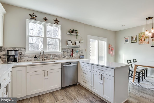 kitchen featuring light wood-style floors, dishwasher, a peninsula, and a sink