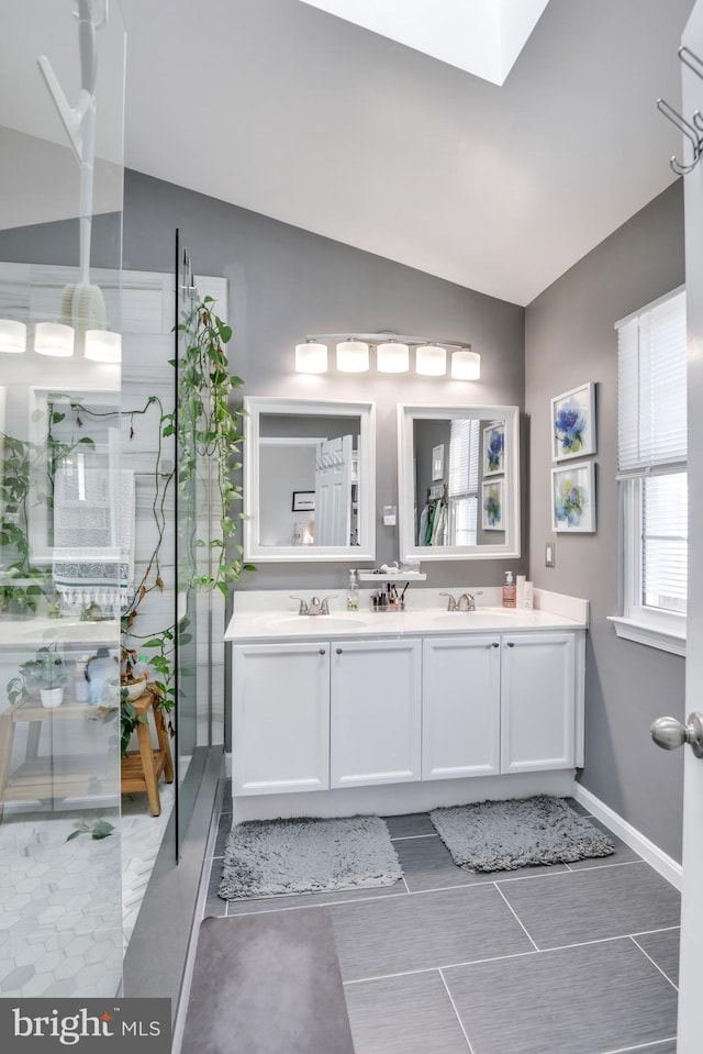 bathroom featuring vaulted ceiling with skylight, double vanity, walk in shower, and a sink