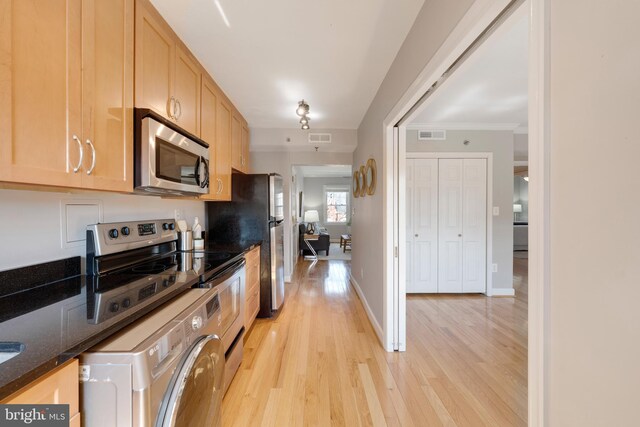 kitchen featuring light brown cabinets, dark stone countertops, stainless steel appliances, light wood-style floors, and baseboards