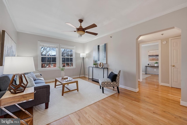 living area with arched walkways, light wood-type flooring, baseboards, and ornamental molding