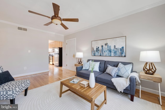 living area featuring visible vents, baseboards, light wood-style floors, and ornamental molding