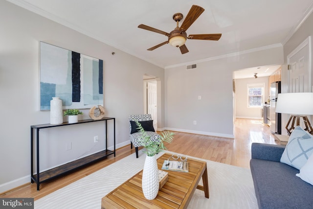 living room with light wood finished floors, visible vents, crown molding, and baseboards