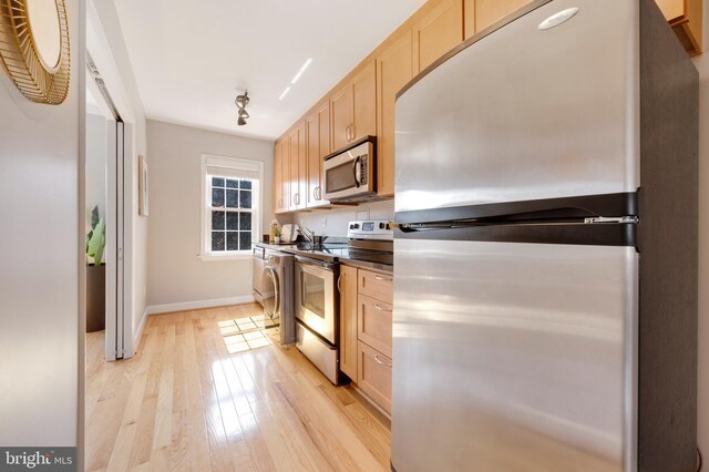 kitchen featuring light brown cabinetry, light wood-style flooring, stainless steel appliances, and dark countertops