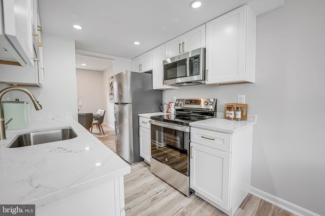 kitchen featuring a sink, light stone countertops, appliances with stainless steel finishes, and light wood-style flooring