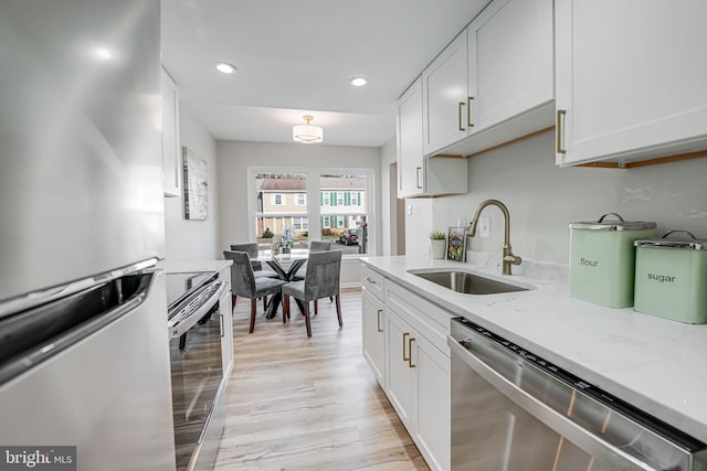 kitchen featuring white cabinets, appliances with stainless steel finishes, light stone countertops, and a sink