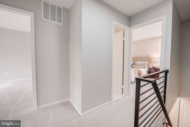 hallway with visible vents, carpet floors, baseboards, and an upstairs landing