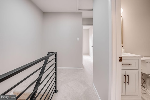 corridor featuring attic access, an upstairs landing, light colored carpet, and baseboards