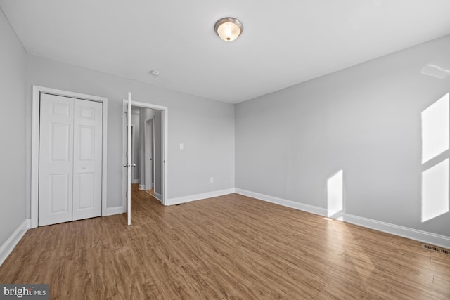 unfurnished bedroom with a closet, visible vents, baseboards, and wood finished floors