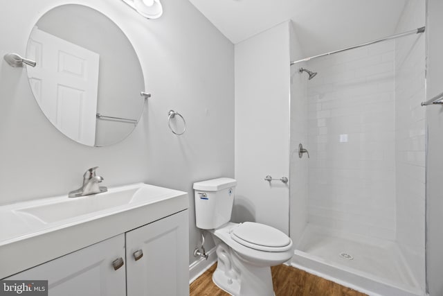 bathroom with toilet, a tile shower, wood finished floors, and vanity