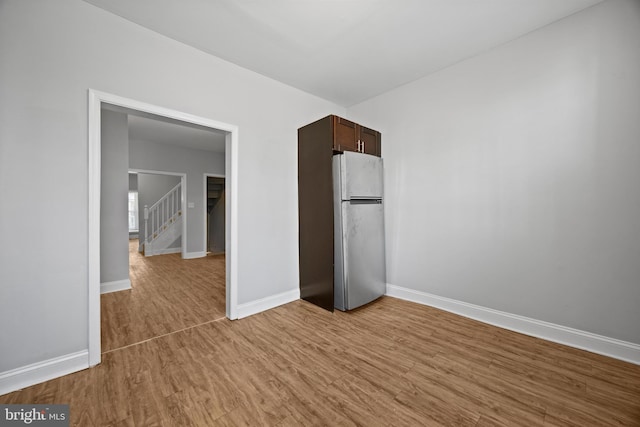 unfurnished bedroom with a closet, baseboards, wood finished floors, and freestanding refrigerator