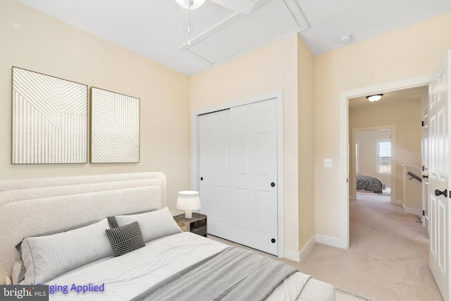 bedroom with a closet, light colored carpet, attic access, and baseboards