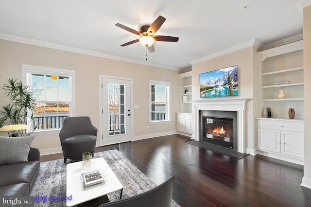 living area with a fireplace with flush hearth, crown molding, baseboards, ceiling fan, and dark wood-style flooring