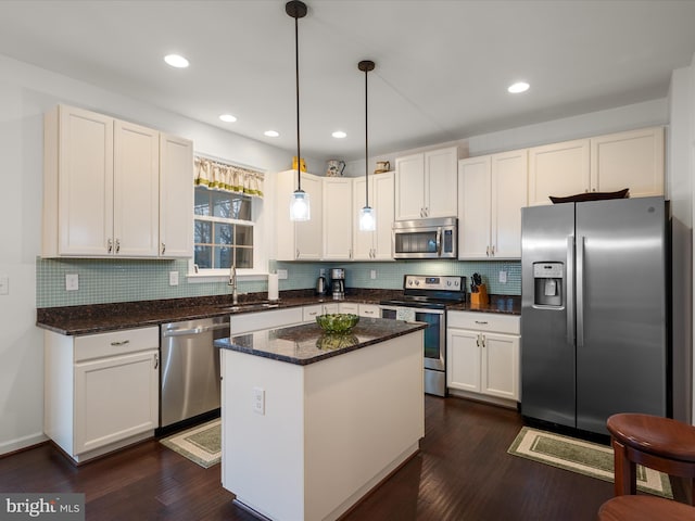 kitchen featuring white cabinets, dark wood finished floors, appliances with stainless steel finishes, decorative light fixtures, and a sink