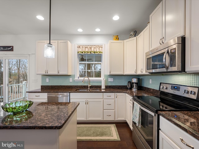 kitchen featuring dark wood finished floors, stainless steel appliances, backsplash, a sink, and dark stone countertops