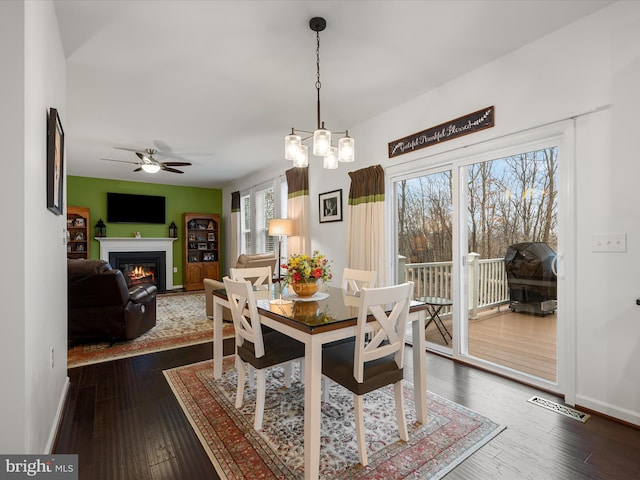 dining area with baseboards, visible vents, a glass covered fireplace, dark wood-style floors, and ceiling fan with notable chandelier