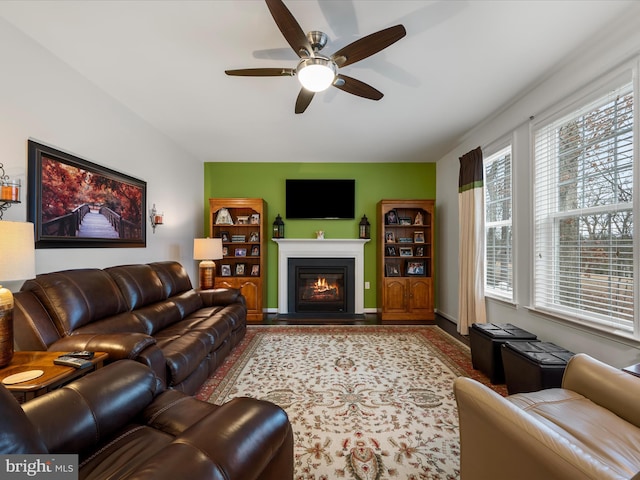 living room featuring a glass covered fireplace, ceiling fan, and baseboards