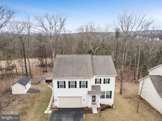 view of front of home featuring aphalt driveway, a garage, an outdoor structure, roof with shingles, and a forest view