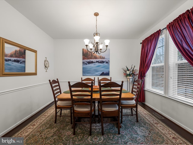 dining area featuring baseboards, visible vents, a chandelier, and wood finished floors