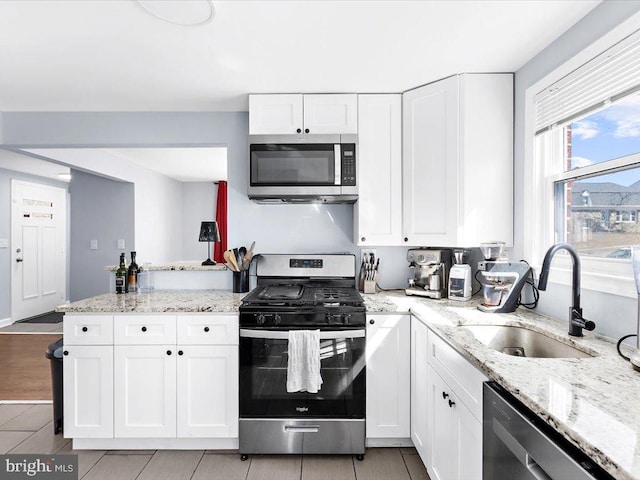 kitchen with a peninsula, white cabinetry, appliances with stainless steel finishes, and a sink