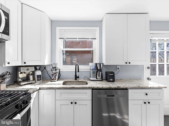 kitchen featuring stainless steel appliances, a sink, white cabinetry, and light stone countertops