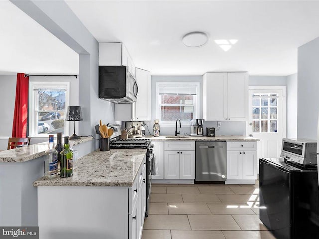 kitchen featuring plenty of natural light, appliances with stainless steel finishes, light stone counters, white cabinetry, and a sink