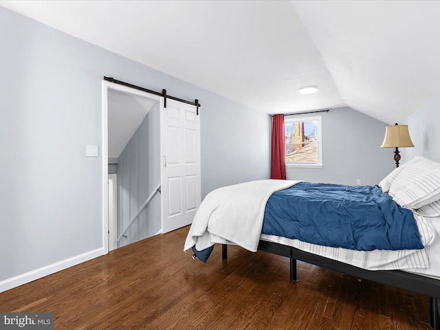 bedroom featuring wood finished floors, vaulted ceiling, baseboards, and a barn door