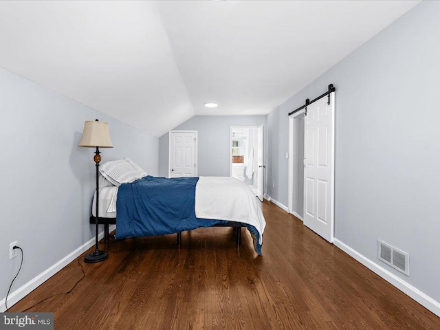 bedroom featuring a barn door, visible vents, vaulted ceiling, and wood finished floors