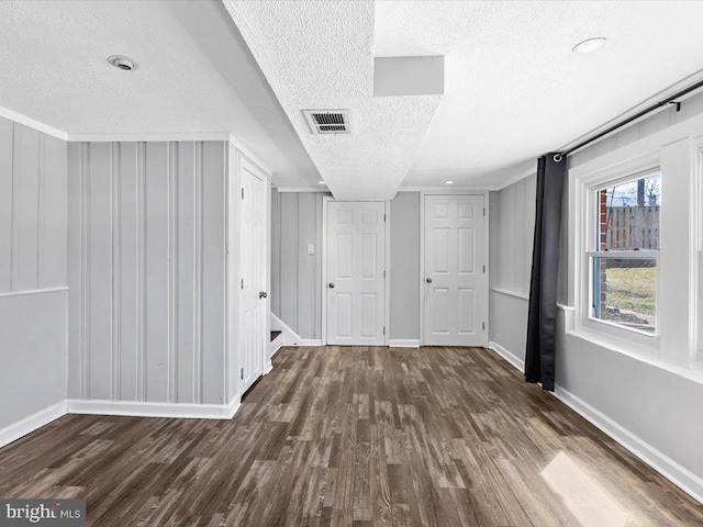 interior space with a textured ceiling, dark wood finished floors, visible vents, and baseboards