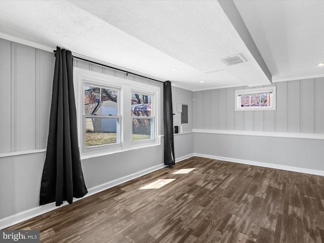 unfurnished room featuring a textured ceiling, wood finished floors, visible vents, baseboards, and electric panel