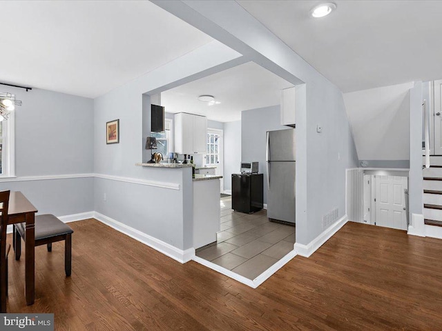 interior space featuring freestanding refrigerator, white cabinetry, baseboards, and wood finished floors