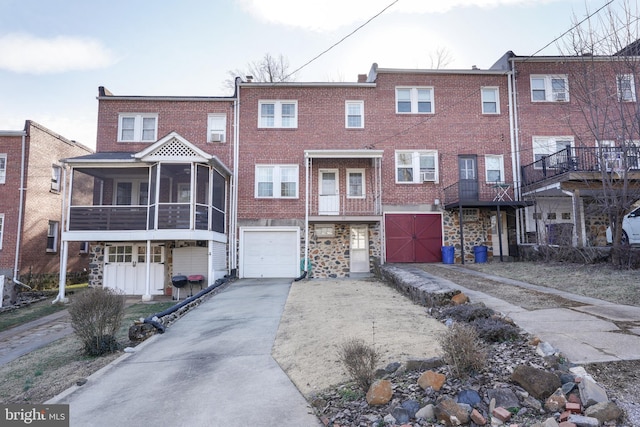 multi unit property with driveway, a garage, a sunroom, stone siding, and brick siding