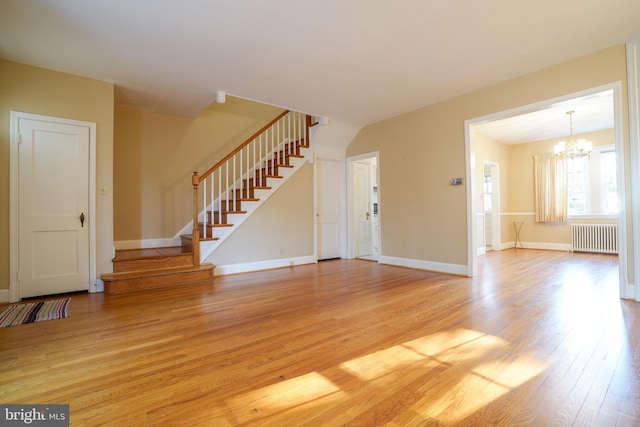 unfurnished living room with baseboards, radiator heating unit, stairway, an inviting chandelier, and light wood-type flooring