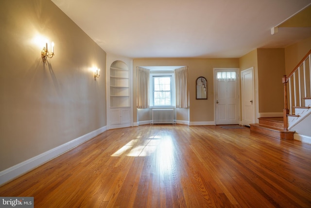 foyer featuring wood finished floors, baseboards, radiator heating unit, and stairs