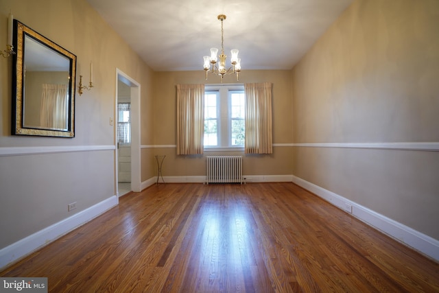 empty room with baseboards, a notable chandelier, radiator heating unit, and wood finished floors