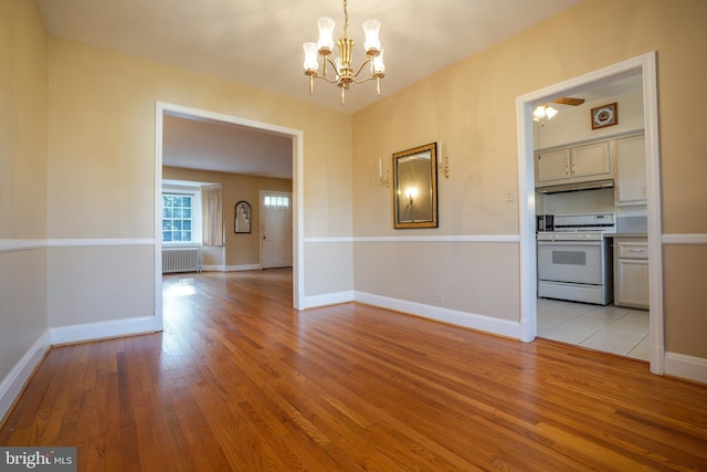 unfurnished dining area featuring a chandelier, light wood-type flooring, baseboards, and radiator heating unit