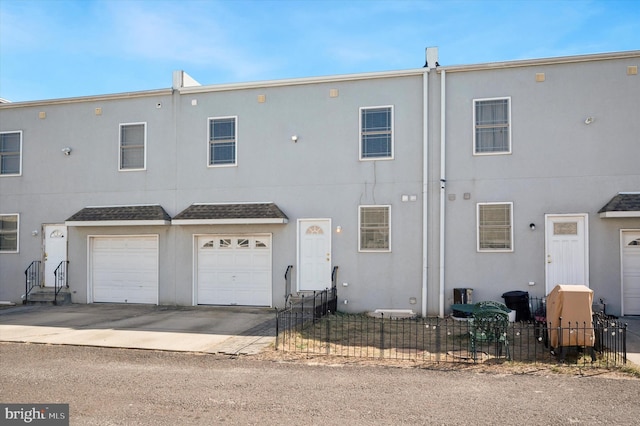 back of house with roof with shingles, stucco siding, concrete driveway, an attached garage, and fence