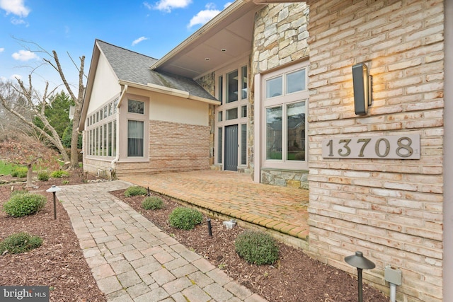 rear view of house featuring a patio area, a shingled roof, brick siding, and stucco siding