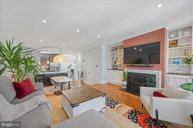 living area featuring built in shelves, a fireplace with flush hearth, recessed lighting, light wood-style floors, and baseboards