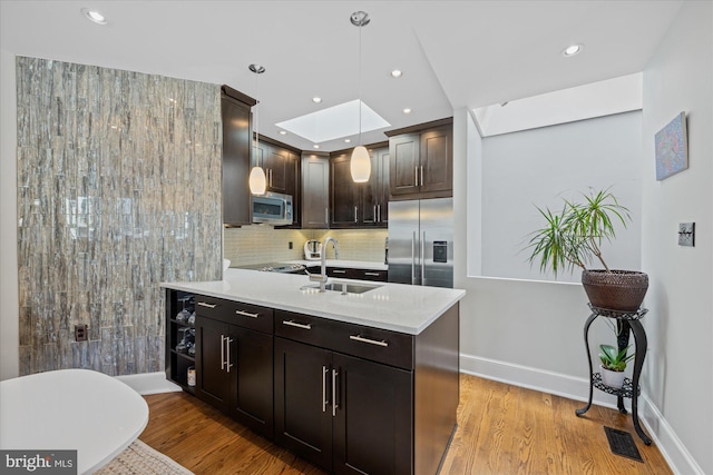 kitchen with dark brown cabinetry, light countertops, appliances with stainless steel finishes, a skylight, and a sink