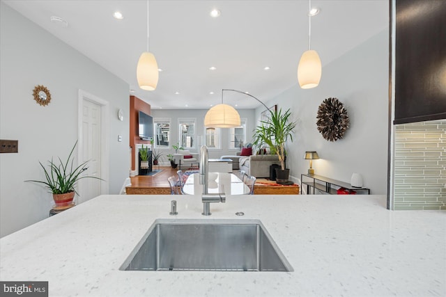 kitchen with a sink, light stone countertops, pendant lighting, and recessed lighting