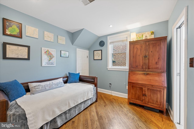 bedroom featuring visible vents, light wood-type flooring, baseboards, and vaulted ceiling