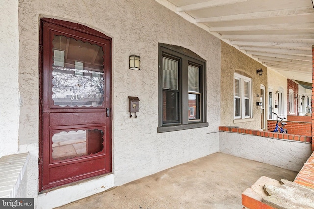 doorway to property featuring covered porch and stucco siding