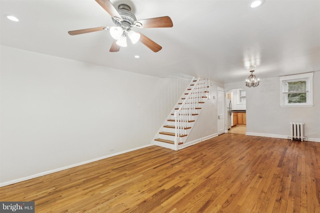 unfurnished living room featuring arched walkways, baseboards, stairs, radiator heating unit, and wood-type flooring