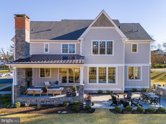 back of property featuring a patio, a chimney, metal roof, a standing seam roof, and board and batten siding